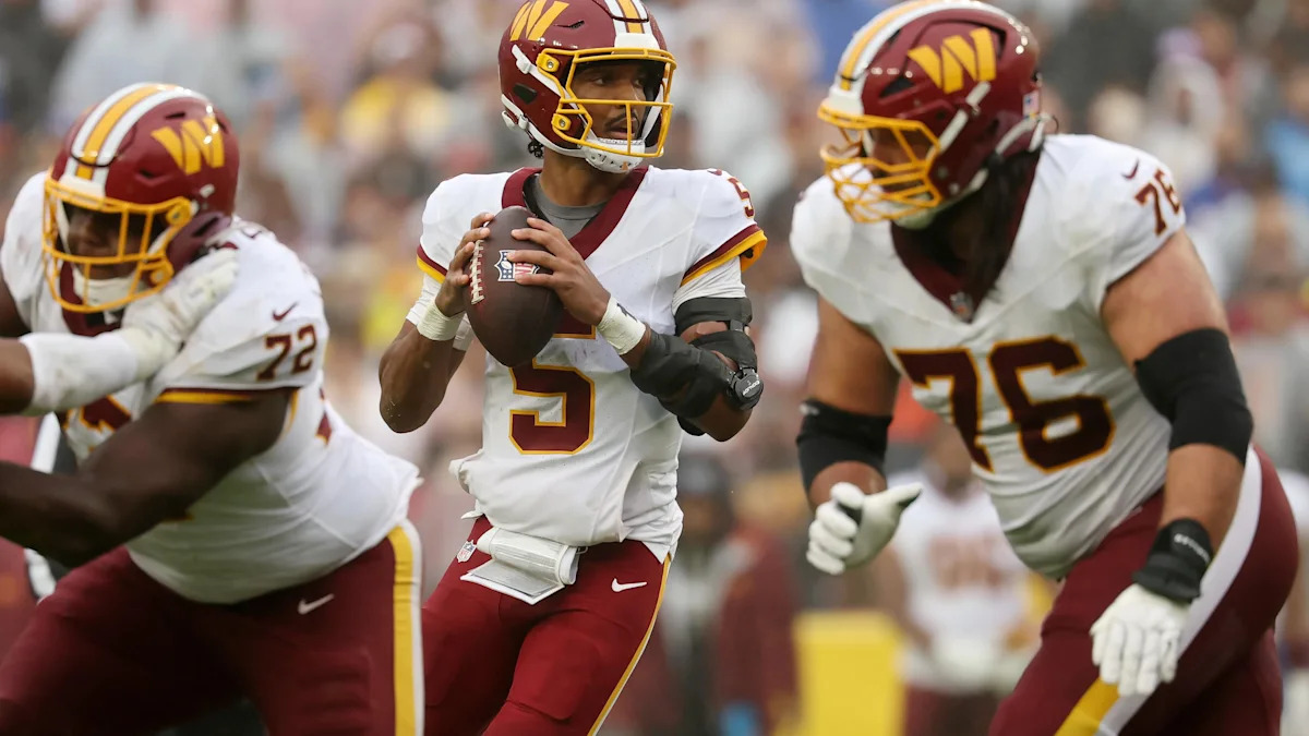 Jayden Daniels carrega a bola entre companheiros do Washington Commanders.