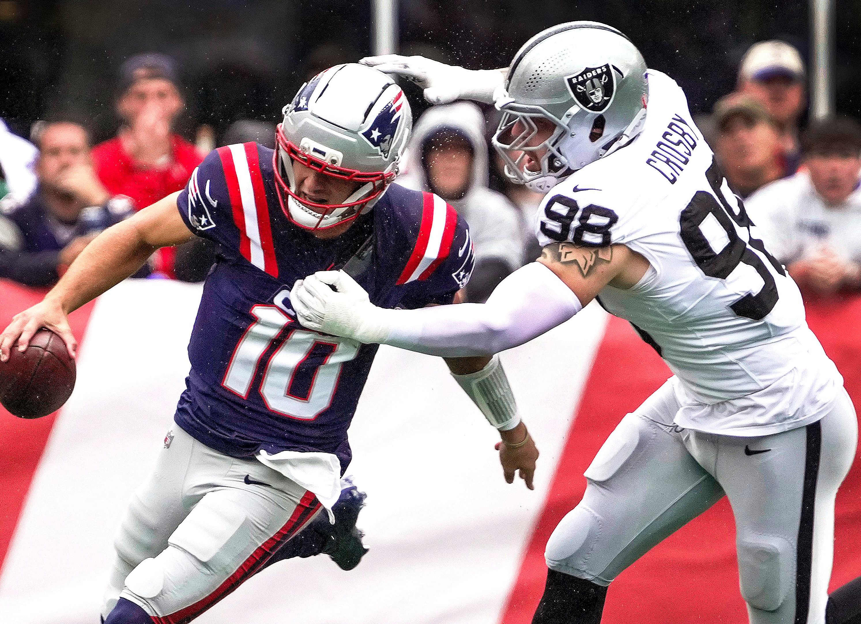Maxx Crosby tenta alcançar Drake Maye em um jogo entre Raiders e Patriots.
