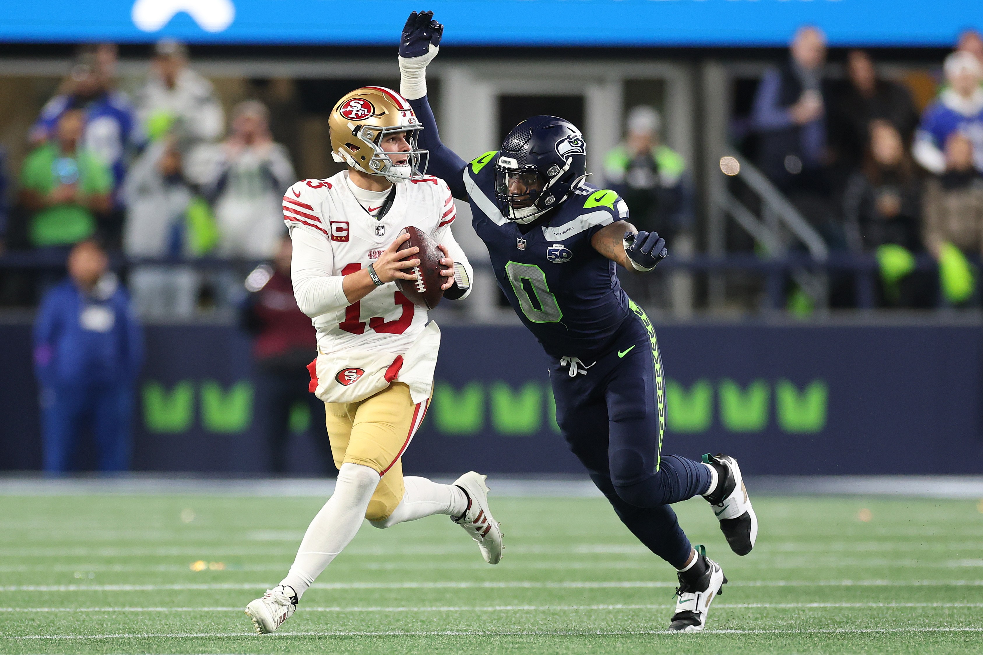 Brock Purdy tenta um passe sob a pressão de um defensor dos Seahawks.