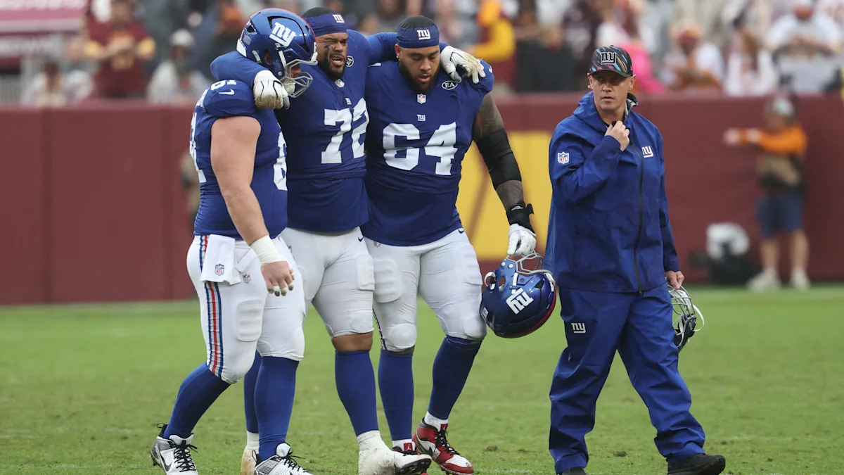 Jogador dos Giants sai de campo acompanhado por integrantes da equipe; imagem relacionada ao relatório de lesões.