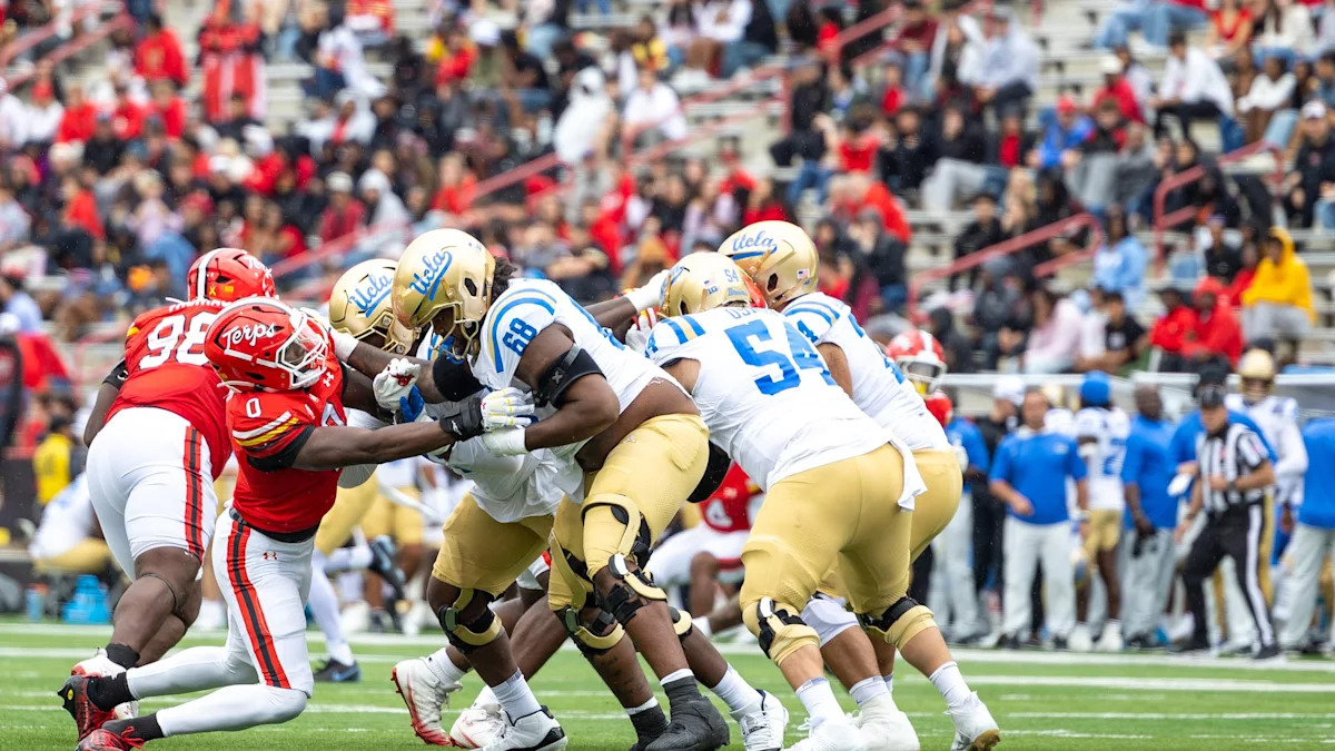 Jogadores de Maryland tentam conter um avanço de UCLA em partida universitária.