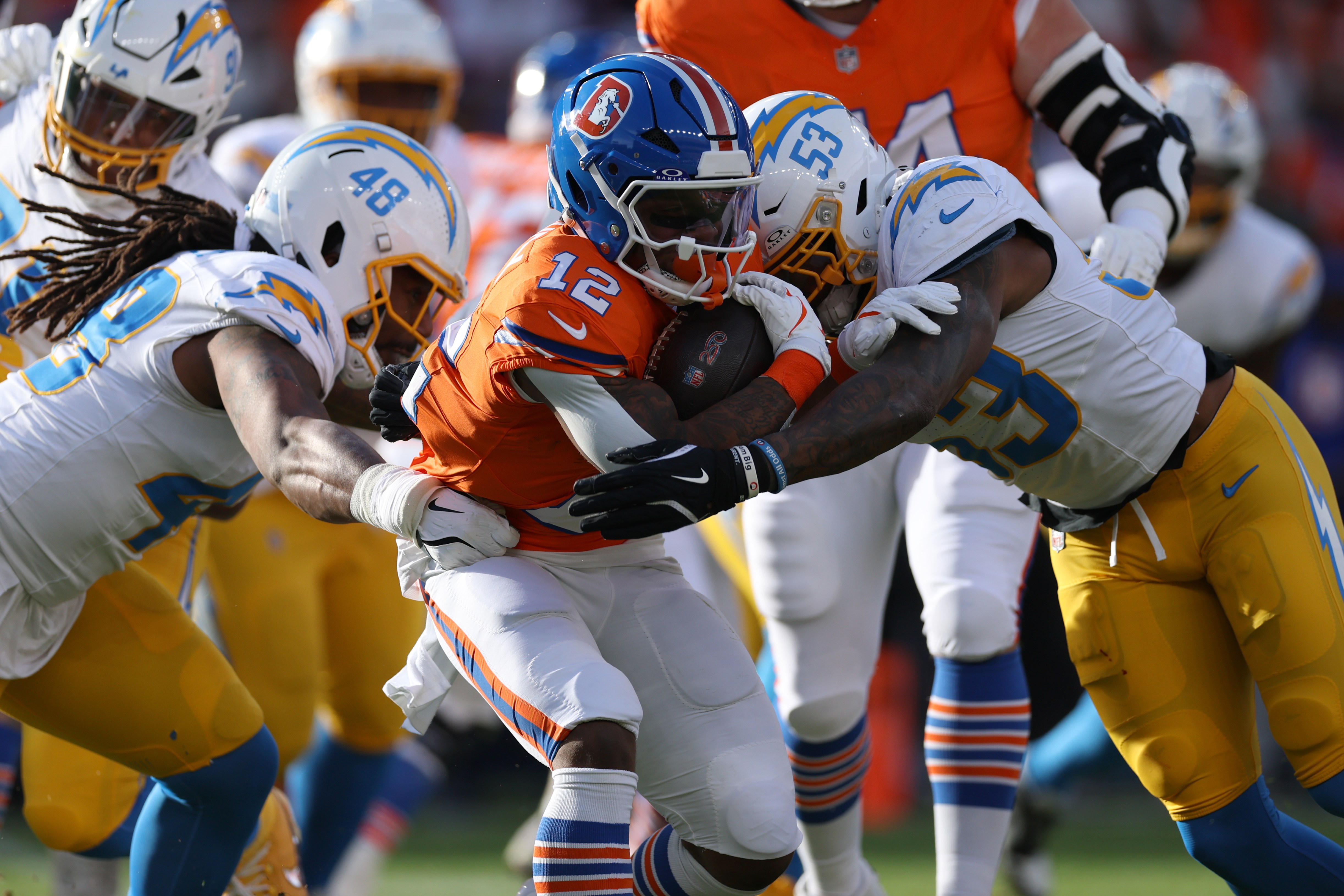 Bud Dupree e Del’shawn Phillips, dos Chargers, derrubam RJ Harvey, dos Broncos, em Denver, em 4 de janeiro de 2026.