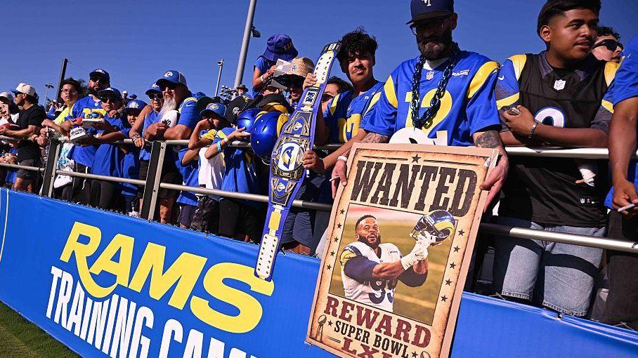 Torcedores dos Rams em treino de pré-temporada; um deles segura um cartaz de Aaron Donald